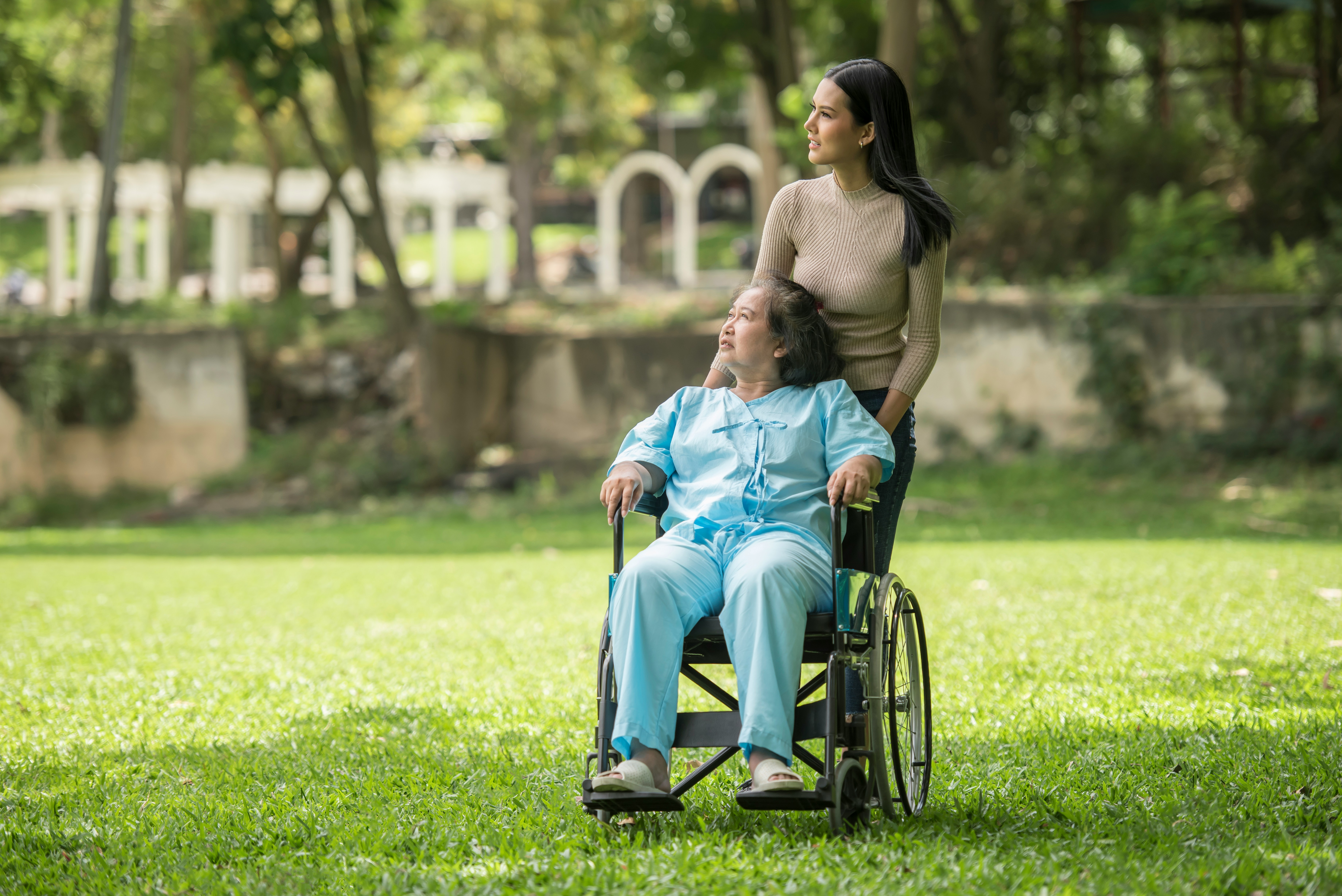 A caregiver strolling through the park with a woman in a wheelchair