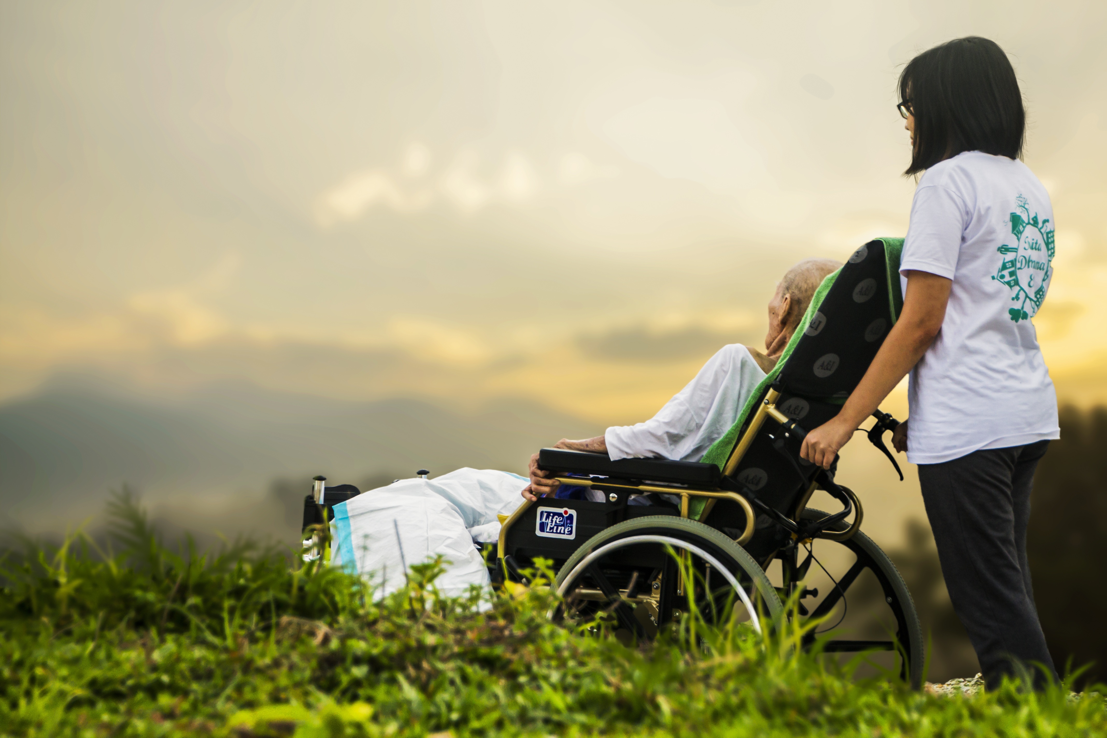 A caregiver and a man in a wheelchair enjoying a sunset outdoors